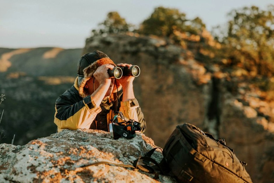 A photographer pauses on a rocky trail with a camera and wide landscape ahead.